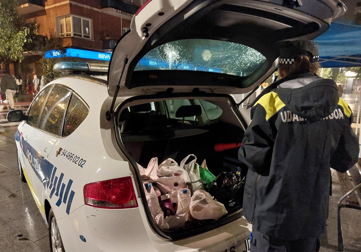 Una agente transporta al vehículo policial las botellas que han sido decomisadas