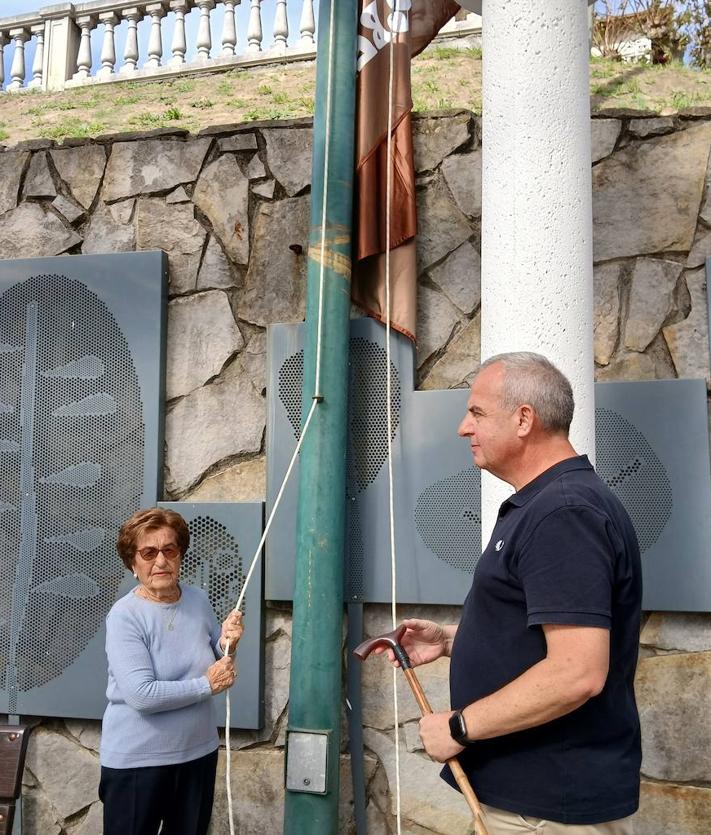 Imagen secundaria 2 - Bisi Fernández, posa sonriente con su nieto, Endika, tras izar la bandera de su pueblo, después de que los vecinos descendieran de la tradicional misa hasta la plaza del Ayuntamiento, donde ha tenido lugar el acto principal de la jornada.