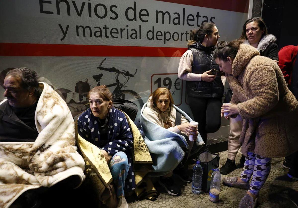 Varias mujeres, tapadas con mantas, aguardan noticias en la calle.