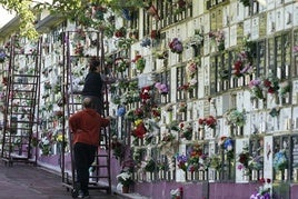 Dos personas engalanan una lápida en el cementerio de Derio.