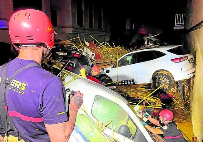 Dos bomberos junto a a coches amontonados.