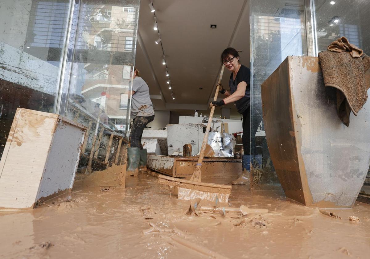 Una mujer extrae agua con lodo de su comercio de Albal.