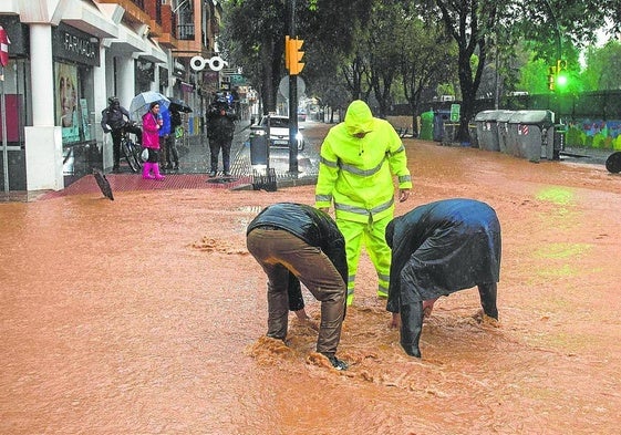 Operarios intentan levantar la tapa de una alcantarilla en una calle inundada de la barriada malagueña de Campanillas.