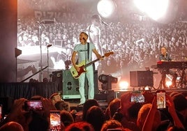 Bryan Adams, con pantalón y camiseta blanca en contraste con su banda enlutada.