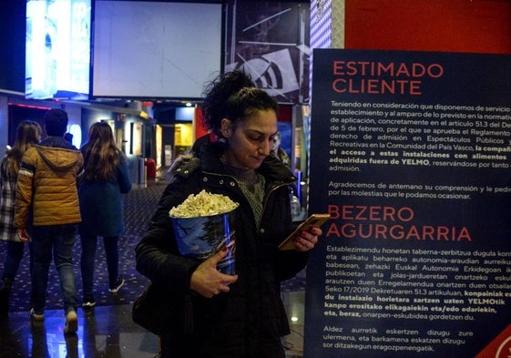 Una joven observa el movil mientras sostiene un cubo de palomitas en el cine de Megapark, en Barakaldo, cuando todavía se prohibía la entrada con productos de fuera.