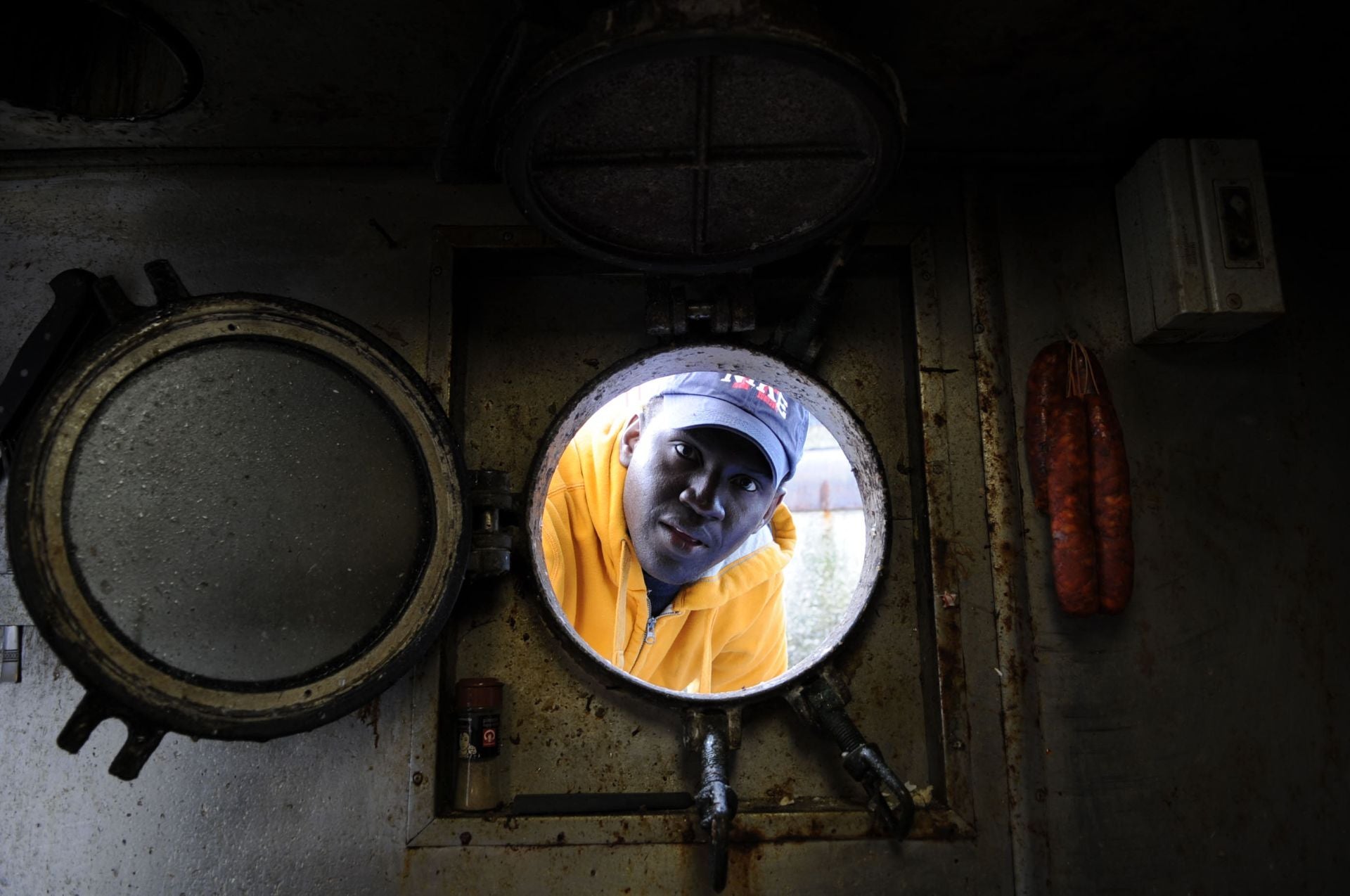 Una senegalés mira por el 'ojo de buey' de un barco del puerto de Ondarroa.