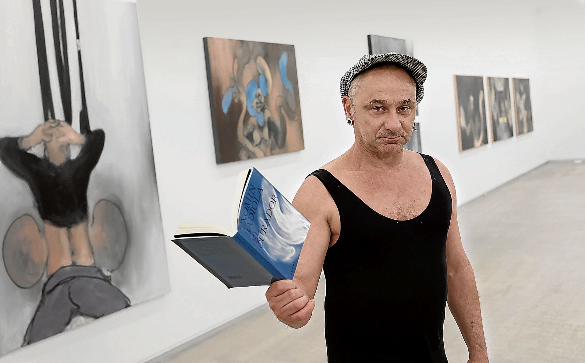 Ignacio Sáez posa en la exposición de sus cuadros 'olvidados', en la galería bilbaína CarrerasMugica. En su mano, la novela de Txomin Badiola, inspirada en ellos.