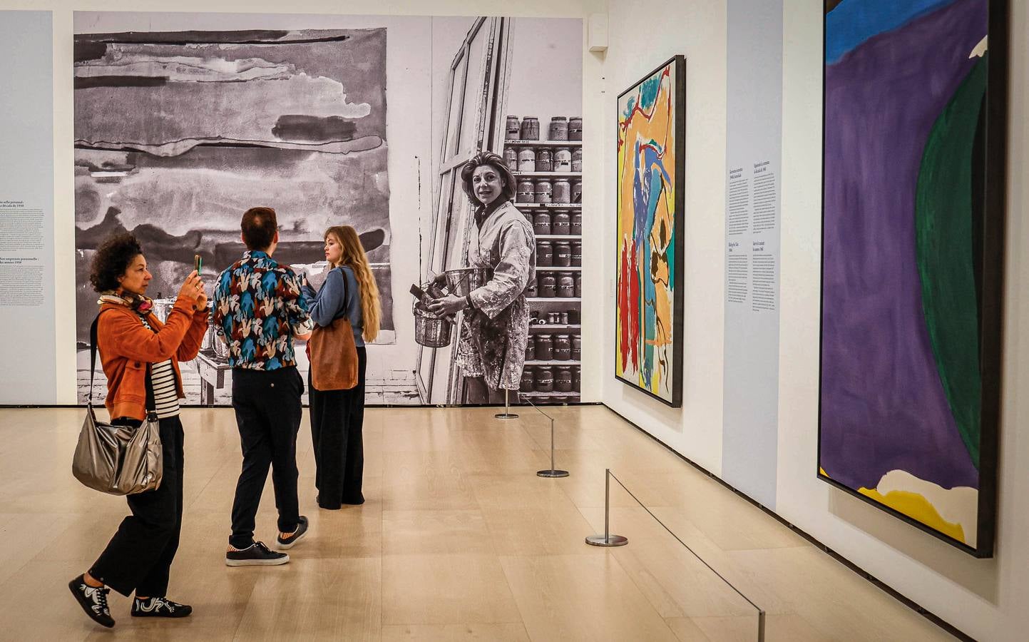 Una zona de la exposición donde puede verse a la artista en una gran foto, junto a los cuadros 'Santorini' (1966), a la derecha de la foto, y 'Pensamientos mediterráneos' (1960).