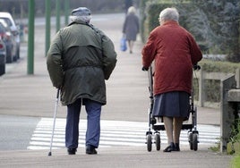 Una pareja de ancianos con problemas de movilidad caminan por la calle.