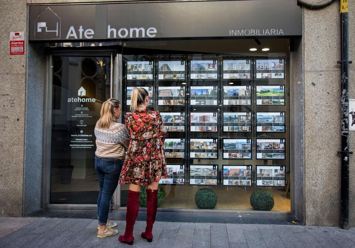 Unas jóvenes se fijan en la oferta de pisos en una inmobiliaria de Bilbao.