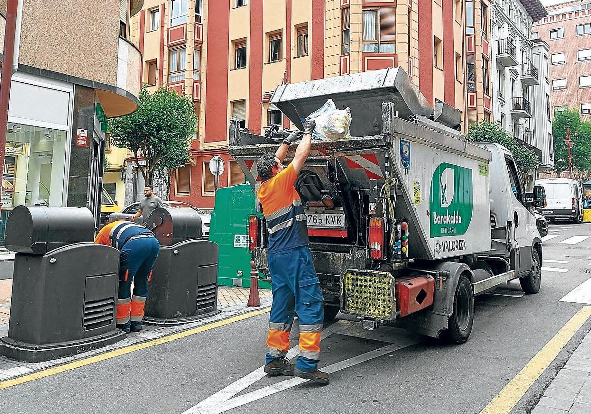 Empleados de la limpieza recogiendo varias bolsas de basura entre unos contenedores en el centro de la localidad.