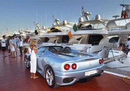 Coche deportivo aparcado junto a yates de lujo en Puerto Banús.