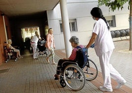 Una trabajadora de una residencia empuja la silla de ruedas de una usuaria.