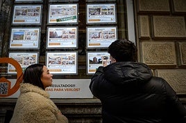 Jóvenes observan los anuncios de una inmobiliaria en Bilbao.