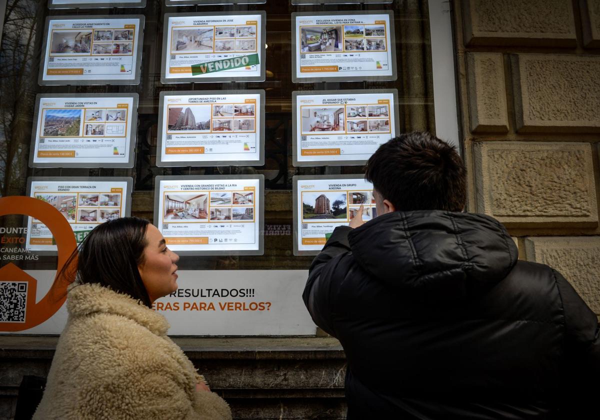 Jóvenes observan los anuncios de una inmobiliaria en Bilbao.