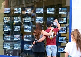 Dos jóvenes, frente a los anuncios de una agencia inmobiliaria.