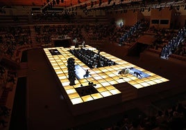 El escenario es una plataforma luminosa (de 30 metros de largo y 12 de ancho) con un foso en el centro que acoge la orquesta.