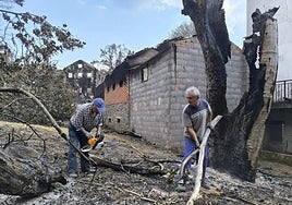 Pedro y Toño cortan los troncos quemados que han caído sobre su casa en San Vicente de Leira.
