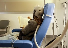 Nerea lee un libro durante la sesión de quimioterapia. En la cabeza lleva el gorro de frío para preservar su cabello.