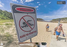 Dos personas abandonan la playa de Galizano, donde un cartel indica la prohibición de bañarse por contaminación.