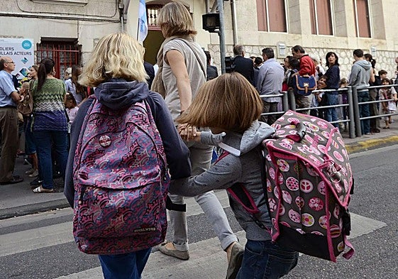 Dos niñas cruzan la calle con su madre para dirigirse a la entrada de la escuela.