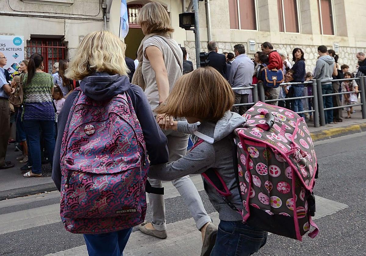 Dos niñas cruzan la calle con su madre para dirigirse a la entrada de la escuela.