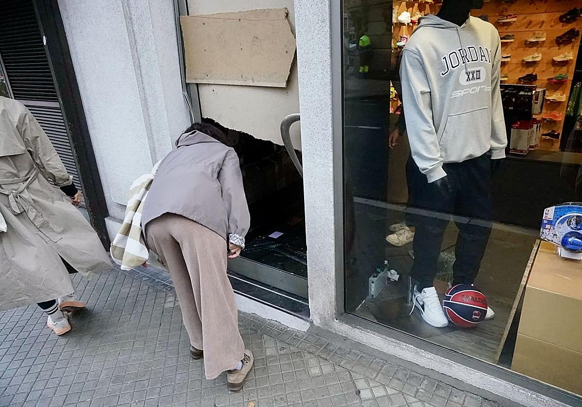 Una transeúnte observa el interior de la tienda asaltada esta madrugada de jueves en la calle Manuel Iradier.
