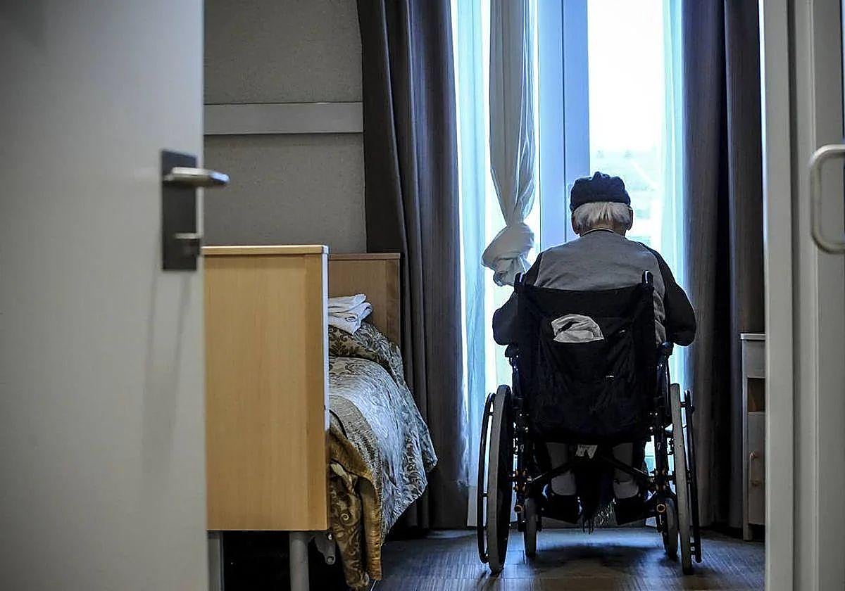 Un mayor dependiente observa por la ventana de una residencia.