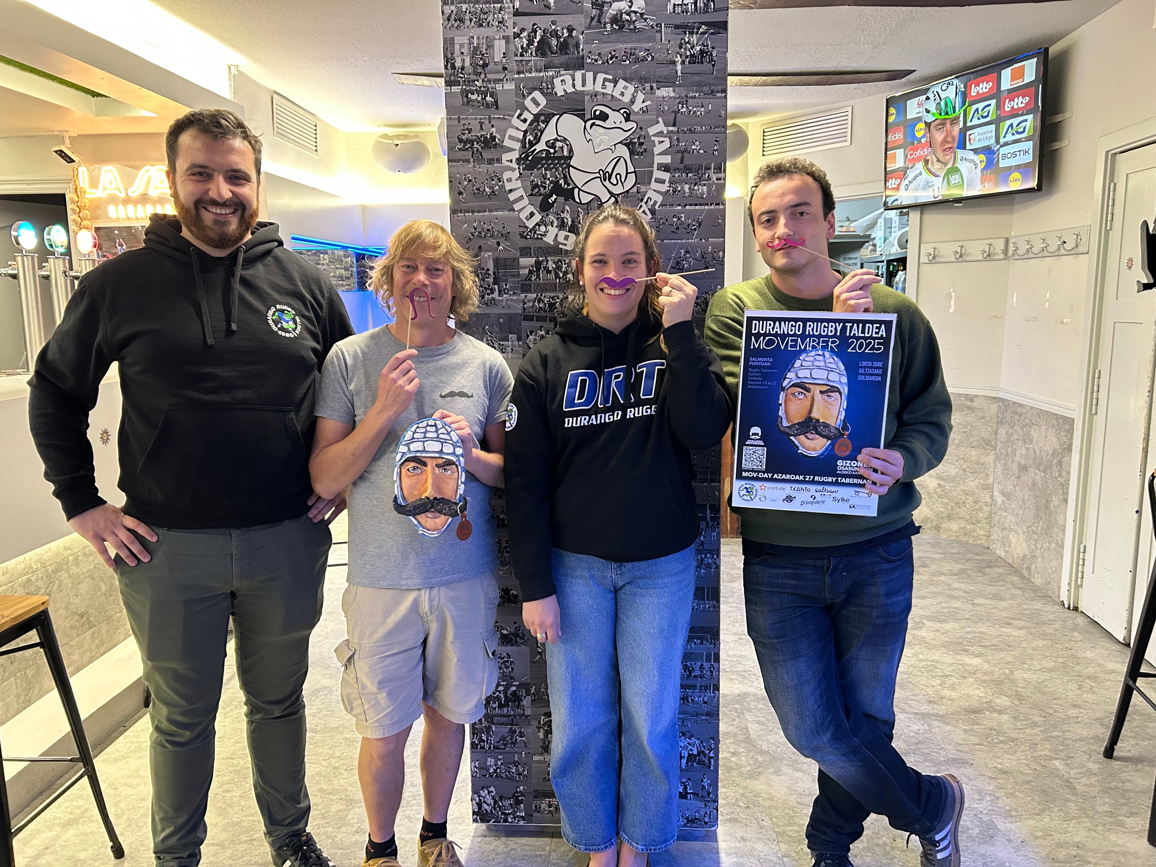 Miembros del club posan con los bigotes y el cartel de la iniciativa solidaria.