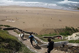 Varios surfistas descienden por las serpenteantes escaleras que llevan a Barinatxe.