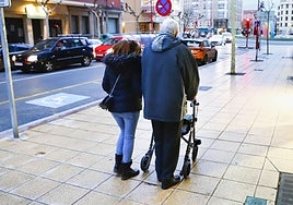 Una persona mayor camina por la calle junto a su cuidadora.