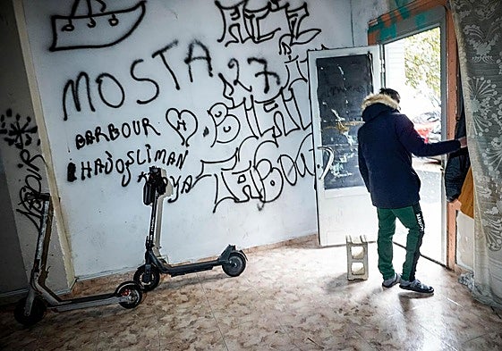 Dos patinetes en una lonja okupada de Coronación. En la puerta, un joven que declara «buscar trabajo» y que en su país era «marinero».