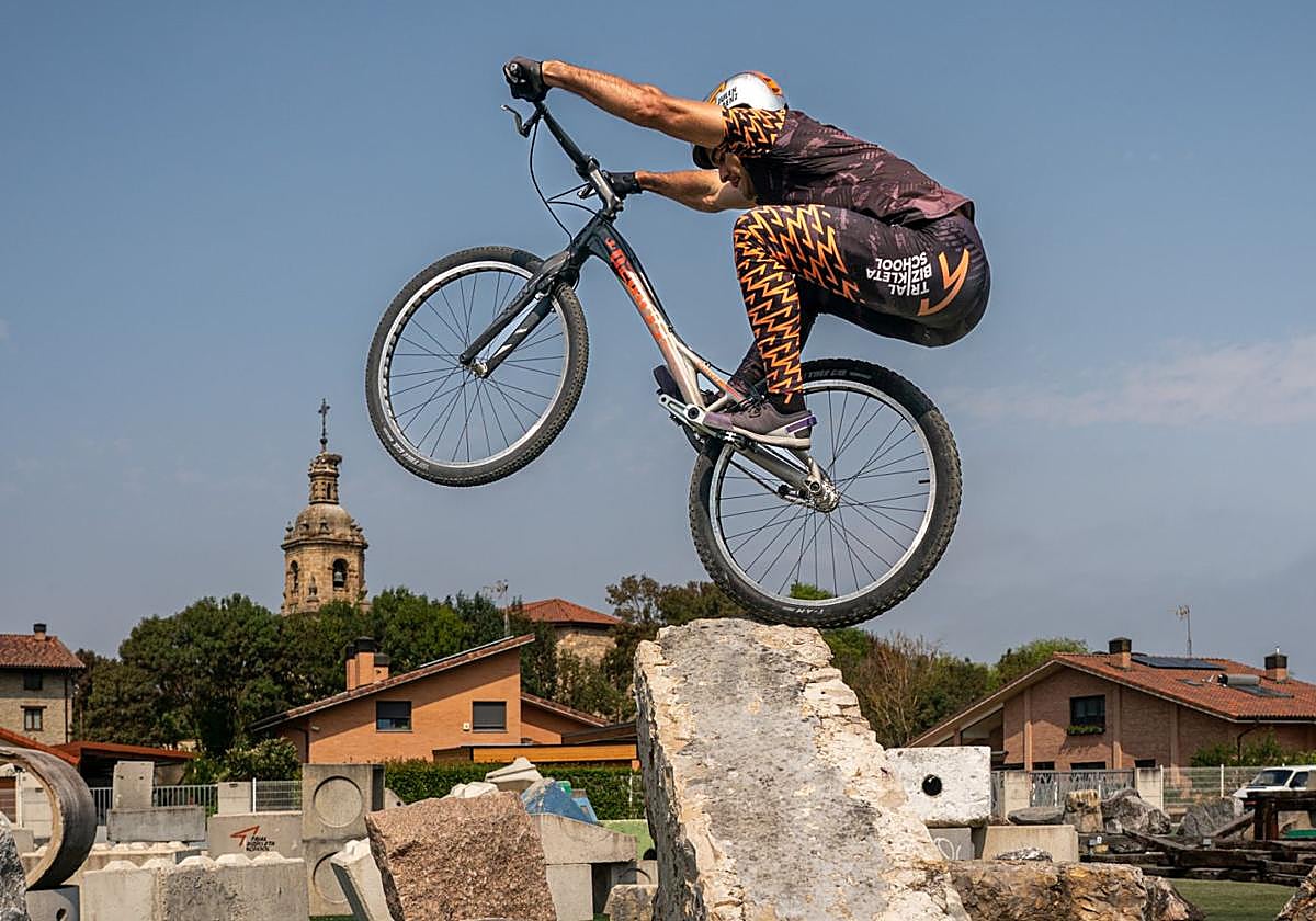 Julen Sáenz de Ormijana sortea obstáculos en el parque de trial de Luko con la iglesia de San Martín Obispo al fondo.