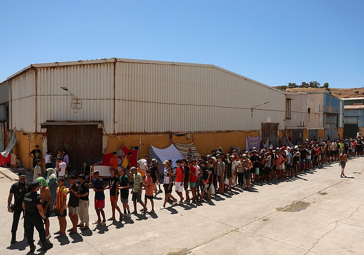 Agentes de la Policía Nacional controlan una fila con menores en una zona de pabellones de Ceuta..