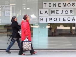 Dos mujeres pasan por delante del anuncio de una sucursal bancaria. / Archivo