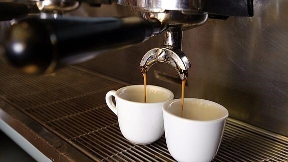Cafetera vierte café en dos tazas.