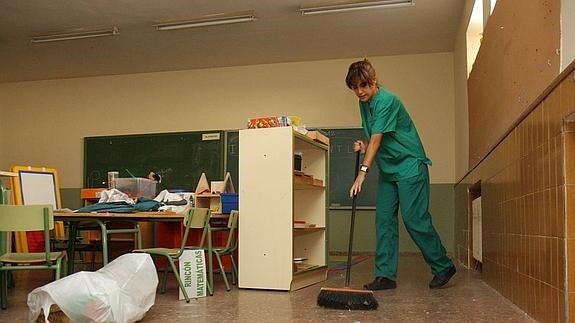 Una empleada barre el suelo de un aula.