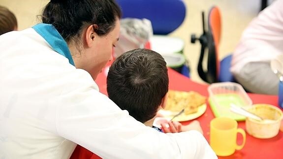 Un niño es ayudado por una auxiliar en un comedor escolar.