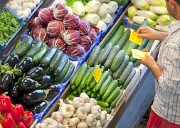Un hombre coloca precios en un surtido de vegetales en un supermercado.