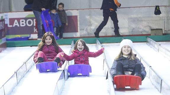Varias niñas se divireten con los trineos en la pista de hielo instalada en la plaza de la Virgen Blanca