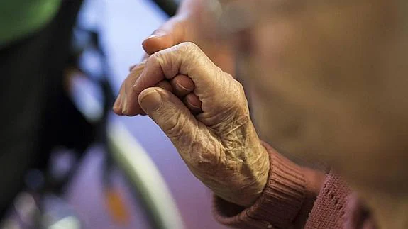 Una sistenta social sostiene la mano de un anciano. 