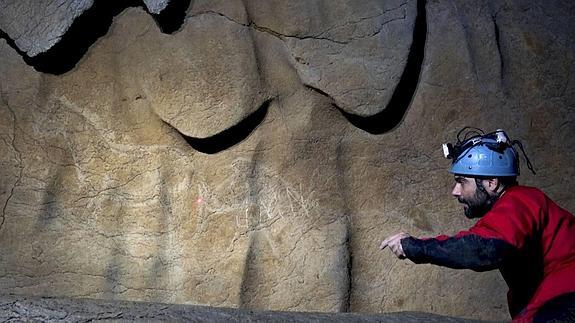 El arqueólogo Diego Garate señala las siluetas de unos caballos, grabados en la roca de la cueva de Atxurra, en Berriatua.