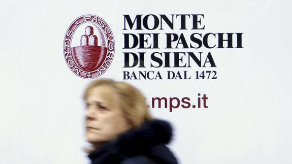 Una mujer camina frente a un banco Monte Dei Paschi en Siena.