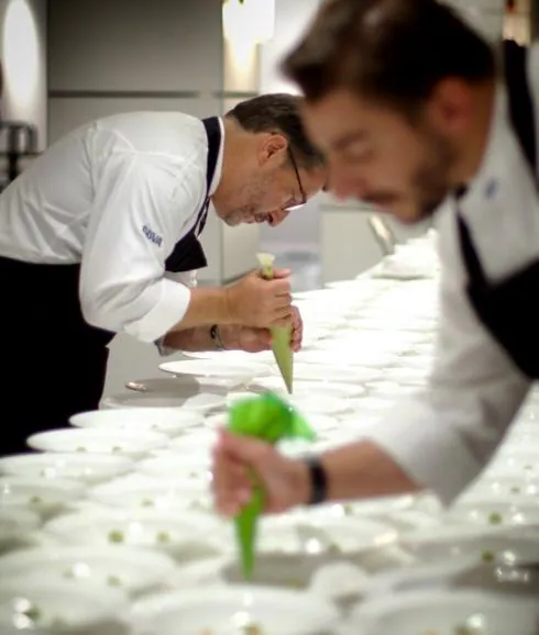 Joan Roca, al fondo, y su hermano Jordi, el repostero, preparan los platos que serán servidos en el menú de una de sus giras por España.