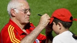 Luis Aragonés, más atento que nunca con los aficionados, firma en la gorra de un joven seguidor español. /EFE