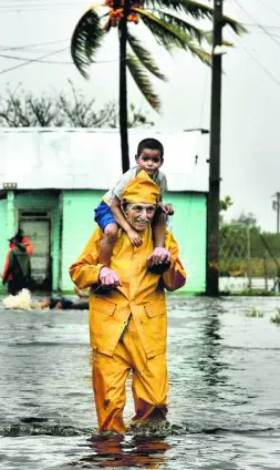 Un cubano atraviesa una calle inundada con su hijo sobre los hombros. / AP