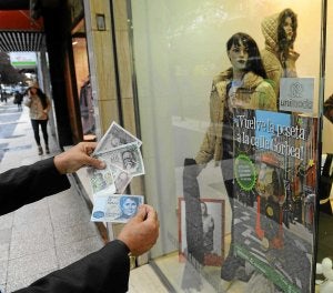 Un cliente muestra pesetas ante un establecimiento. /Igor Aizpuru