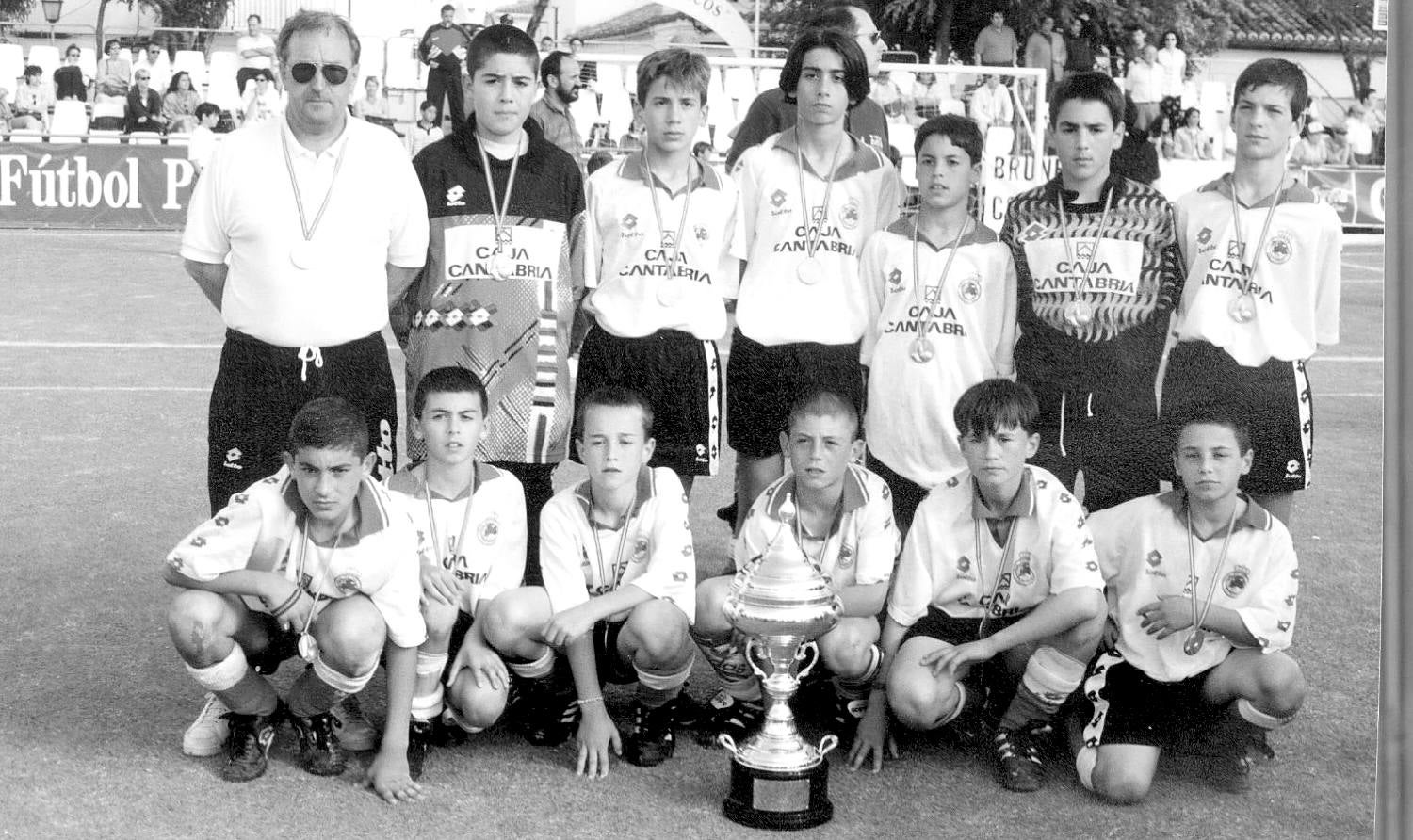 Foto antigua del Racing alevín de la temporada 1996, cuando el equipo se proclamó campeón del Torneo de Brunete. En pie, de izq. a dcha: Nacho Bilbao, entrenador; Carlos López, Alberto Ortiz, Borja Gómez, Manuel Romaña, César Córdoba, Oscar Sáiz. Agachados, de izq. a dcha.: Alvaro Santamaría, Oscar Pérez, Angel de la Peña, Jonathan Valle, Samuel San José y David Alonso.