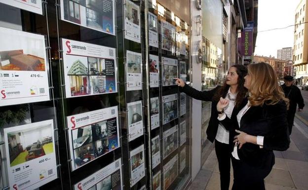 Dos mujeres miran las ofertas del escaparate de la inmobiliaria San Fernando, en Torrelavega.