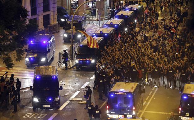 Miembros de los Mossos de Escuadra escoltan la salida de varias furgonetas de la Policia Nacional de la jefatura Superior de Policia de Barcelona, ante la concentración de cientos de personas frente a las dependencias policiales.